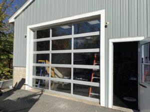 A modern full-view glass garage door installed on a building, showcasing work by Steve Shumsky Unlimited Overhead Doors LLC in Hudson, NH