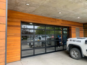 A modern glass garage door installed on a building with wood paneling by Canyon Overhead Doors in Salt Lake City, UT.