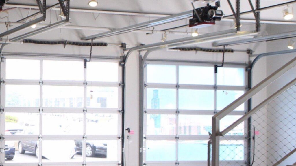 Modern glass garage doors with visible operating mechanisms inside a building by Vertical Door Solutions in Sheridan, WY