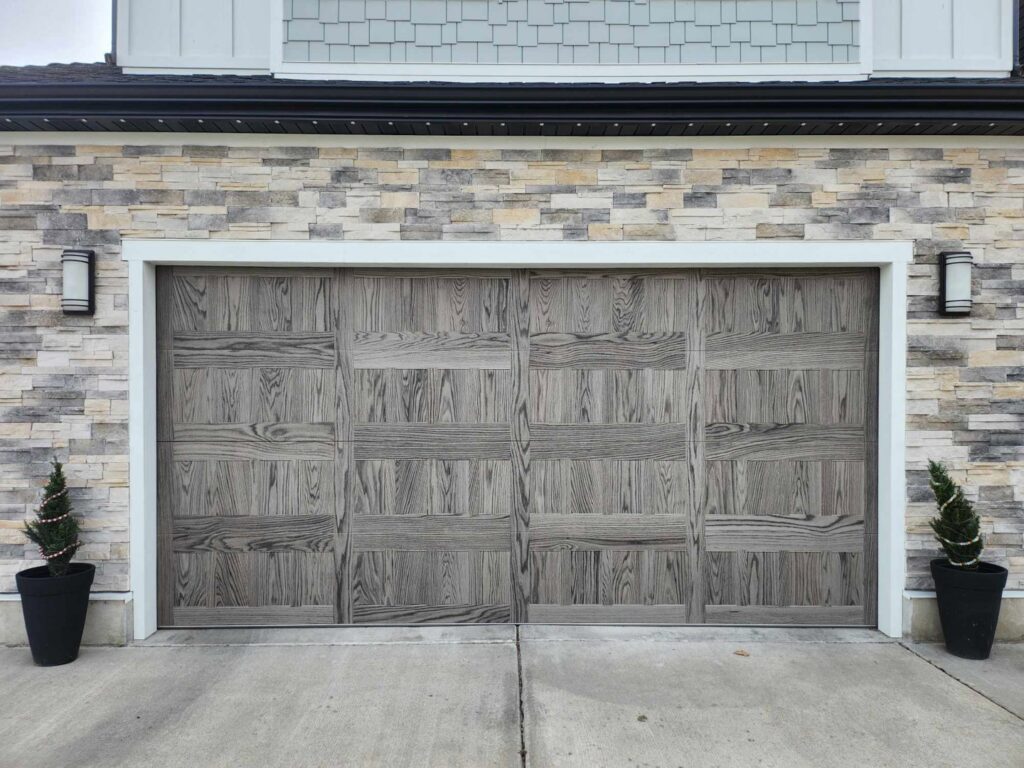 A modern gray wood-look garage door installed on a stone-faced home by Layton Doors in West Jordan, UT.