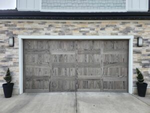 A modern gray wood-look garage door installed on a stone-faced home by Layton Doors in West Jordan, UT.