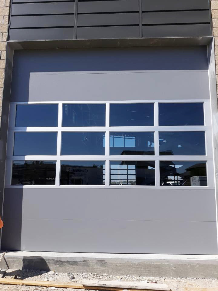 A modern grey garage door with multiple rectangular windows, showcasing an installation by Overhead Door Company of Nampa in Nampa, ID.