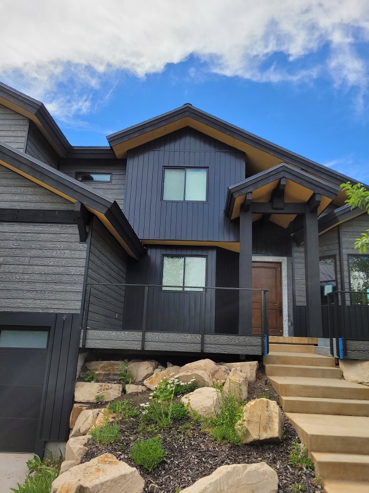 A modern house featuring dark gray vertical siding and natural wood accents, a project by New Look Siding in Midvale, UT.