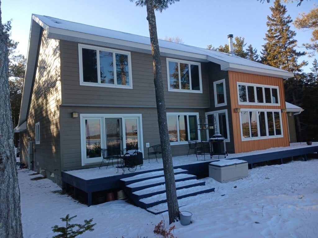 A modern house featuring grey siding and warm wood accents, a project by Murphy Builders- Genesee County in Ossineke, MI.