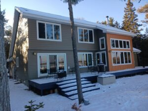 A modern house featuring grey siding and warm wood accents, a project by Murphy Builders- Genesee County in Ossineke, MI.