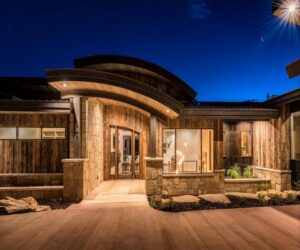 A modern house featuring elegant wood siding and stone accents, beautifully illuminated at night by New Look Siding in Midvale, UT.