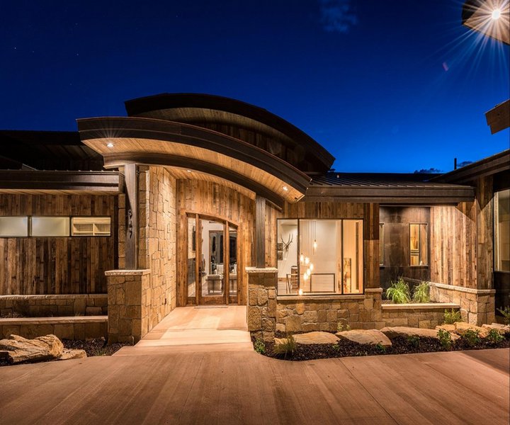 A modern house featuring elegant wood siding and stone accents, beautifully illuminated at night by New Look Siding in Midvale, UT.
