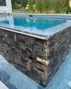 A modern infinity-edge pool with elegant stone tiling by Christman Pool Service in Portland, ME.
