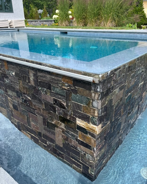 A modern infinity-edge pool with elegant stone tiling by Christman Pool Service in Portland, ME.
