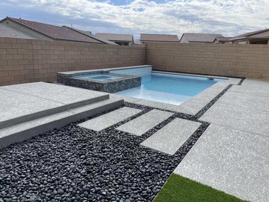 A modern pool and spa area with dark decorative pebbles and stepping stones, built by Steve Breck Pools in Las Vegas, NV.