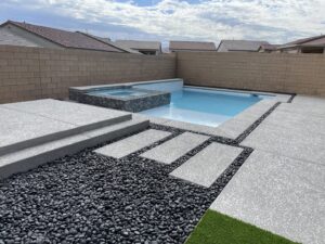 A modern pool and spa area with dark decorative pebbles and stepping stones, built by Steve Breck Pools in Las Vegas, NV.