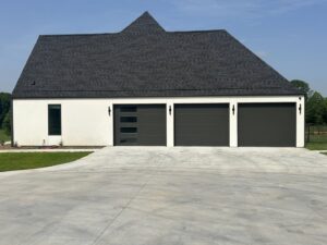 Three modern dark gray garage doors, one with windows, installed on a white residential home by Coney's Garage Doors in Conway, AR.