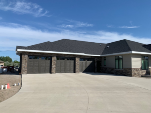 Exterior view of a modern home featuring three dark-colored residential garage doors installed by McCody Overhead Doors in Williston, ND