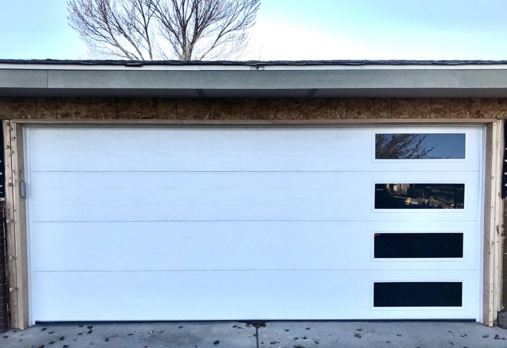 A modern white garage door with horizontal black windows being installed on a new construction by Precision Garage Door of Albuquerque and Santa Fe, NM.