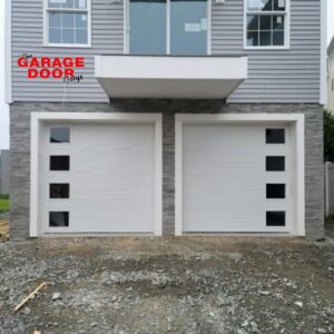 Two modern white garage doors with square windows installed on a grey-sided house by The Garage Door Guys, LLC in New Haven, CT.
