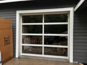 A modern white full-view glass garage door on the exterior of a grey home, installed by Over The Top Garage in Albuquerque, NM.