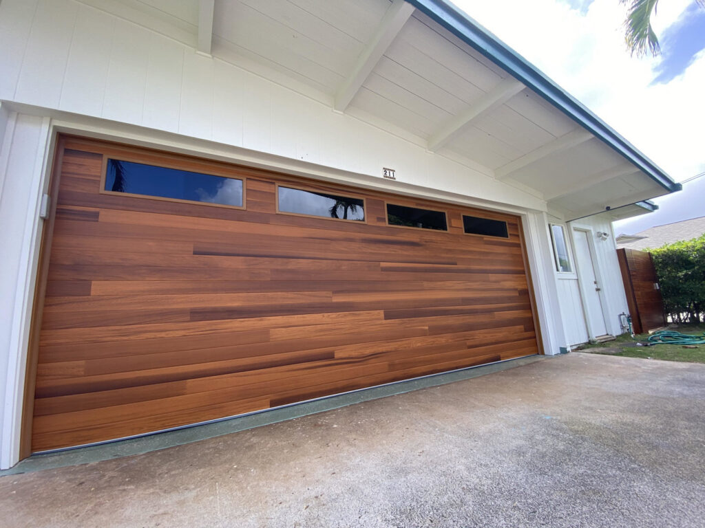 A newly installed modern wood-look garage door with windows by Oahu Garage Doors in Waipahu, HI