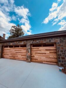 Two modern wood panel garage doors with horizontal slats and windows installed on a stone house by Coney's Garage Doors in Conway, AR.