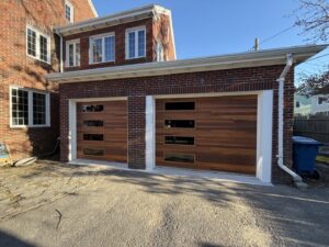 Two modern wooden-style garage doors with horizontal windows installed on a brick home by NDI Garage Door in Plaistow, NH.
