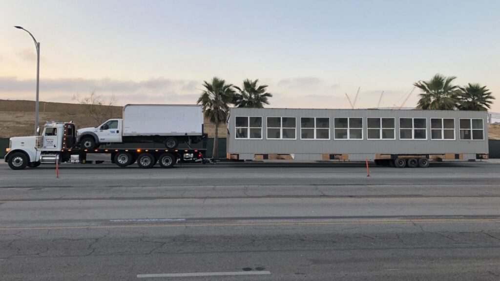 Affordable Towing LLC transporting a long modular building section on a flatbed trailer in Anaheim, CA.