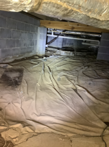 A crawlspace with a dirty, moisture-damaged vapor barrier, indicating water issues for Allied Foundation & Crawlspace Solutions in Decatur, AL.