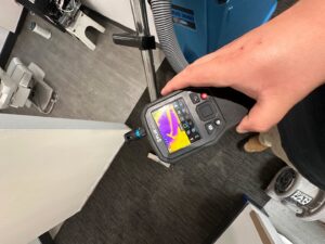 A technician using a thermal camera for moisture detection with drying equipment in the background, by The Recover Tech Restoration in Vancouver, WA.