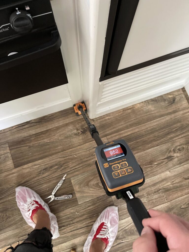 A water damage specialist using a moisture meter to detect hidden water in a hardwood floor, by Elements of Restoration in Denver, CO.