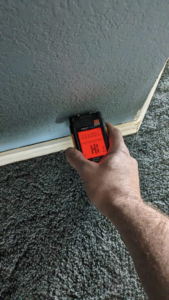 A technician using a moisture meter to detect water damage in a wall for Peak Home Pro Restoration in Clovis, NM.