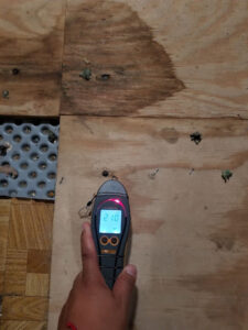 A professional using a moisture meter to check for water damage on a wooden subfloor, performed by A2 Restoration in Ann Arbor, MI.