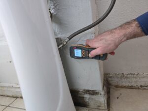 A technician performing a moisture meter inspection for water damage near a toilet at Risk Free Serv Water Damage Repair San Diego, CA