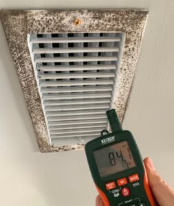 A Restored Air specialist using a moisture meter to assess a moldy air vent, indicating water damage in Summerville, SC.