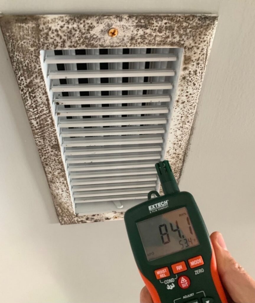 A Restored Air specialist using a moisture meter to assess a moldy air vent, indicating water damage in Summerville, SC.