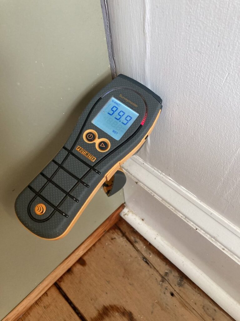 A moisture meter showing 99.9% wet on a wall, indicating severe water damage, used by CleanBright Surface Restoration in Latham, NY.