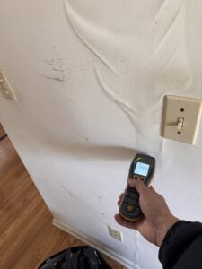 A moisture meter being used to test a water-damaged wall with peeling paint by Island Emergency Disaster Restoration in Farmingdale, NY.
