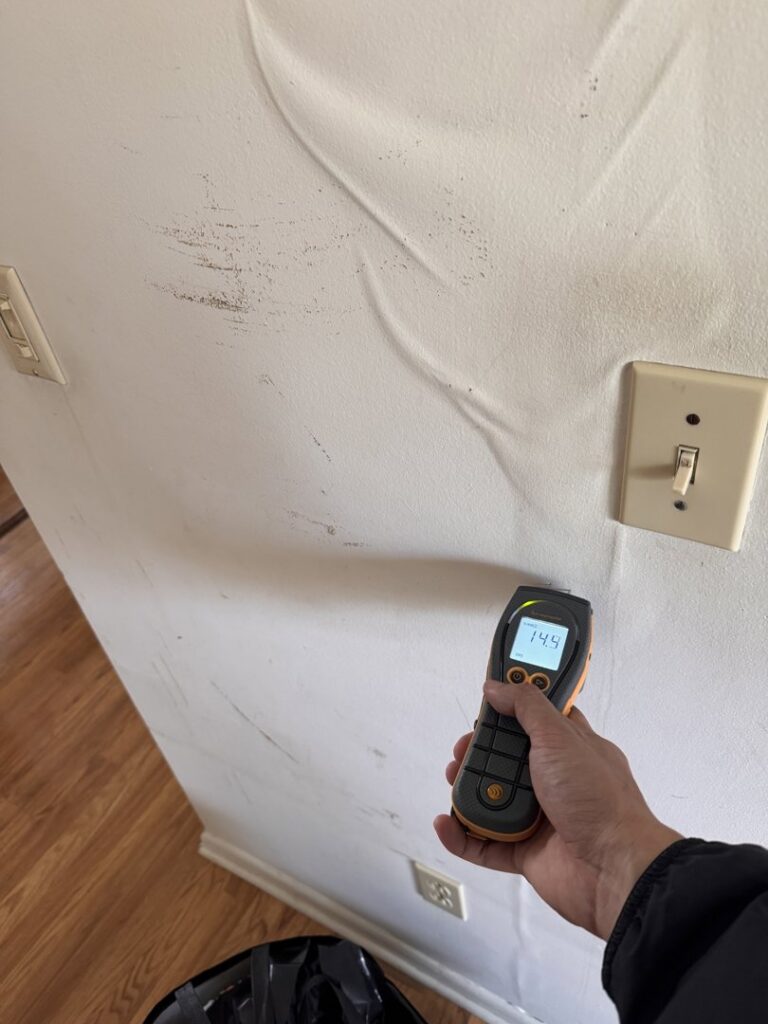A moisture meter being used to test a water-damaged wall with peeling paint by Island Emergency Disaster Restoration in Farmingdale, NY.