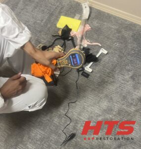 A water damage specialist using a moisture meter on a carpeted floor for assessment by HTS Restoration in El Paso, TX.