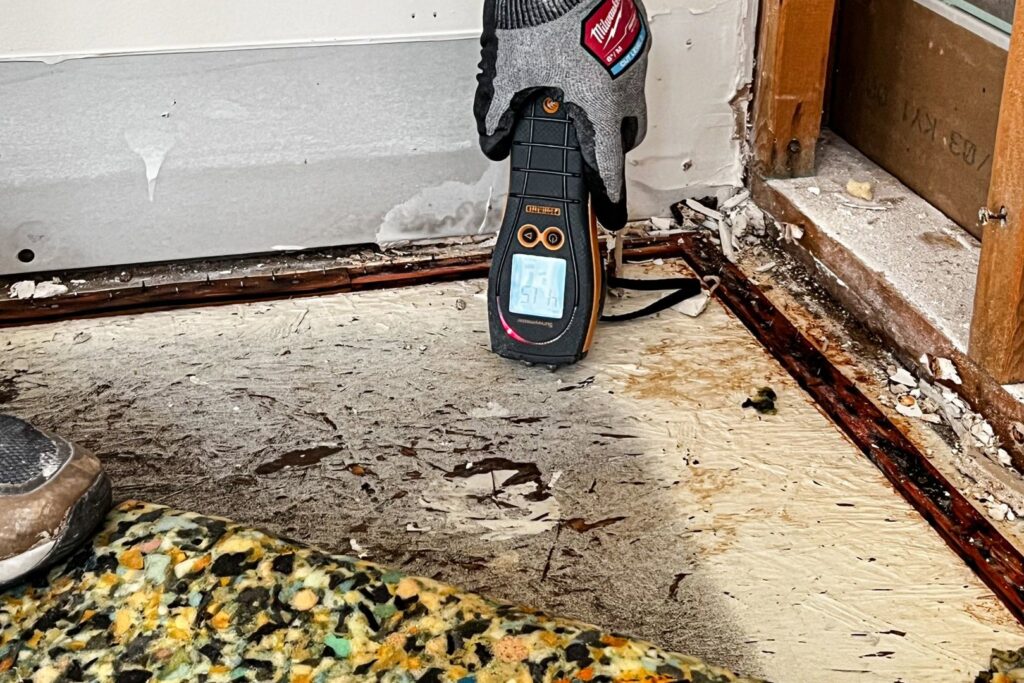 A moisture meter showing a high reading on a damaged floor during water damage assessment by Remont Restoration in Hagerstown, MD.