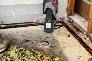 A moisture meter showing a high reading on a damaged floor during water damage assessment by Remont Restoration in Hagerstown, MD.