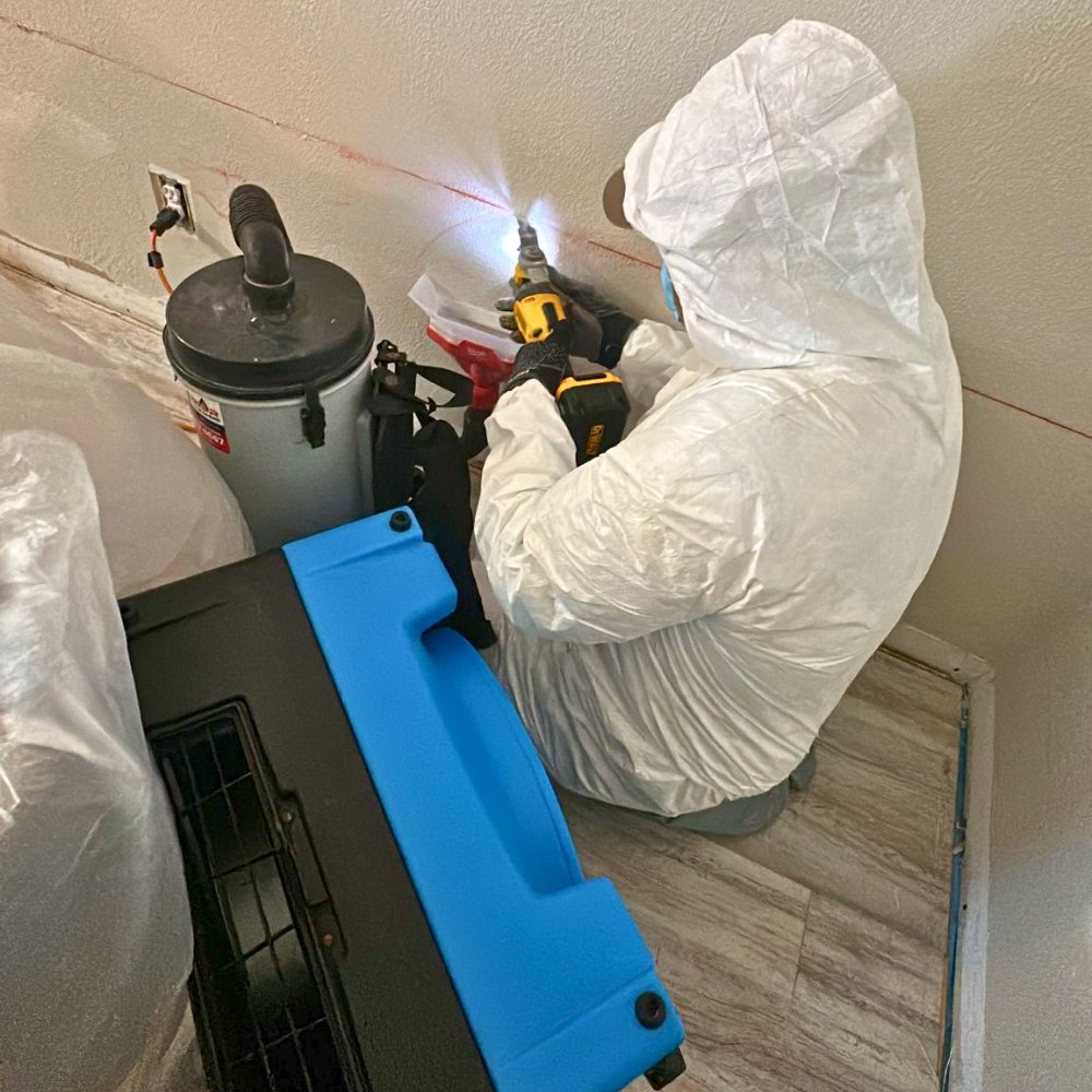 A water damage specialist using a drill for moisture testing or drying a wall with an air mover nearby for Superior Contract Cleaning in Lafayette, LA.