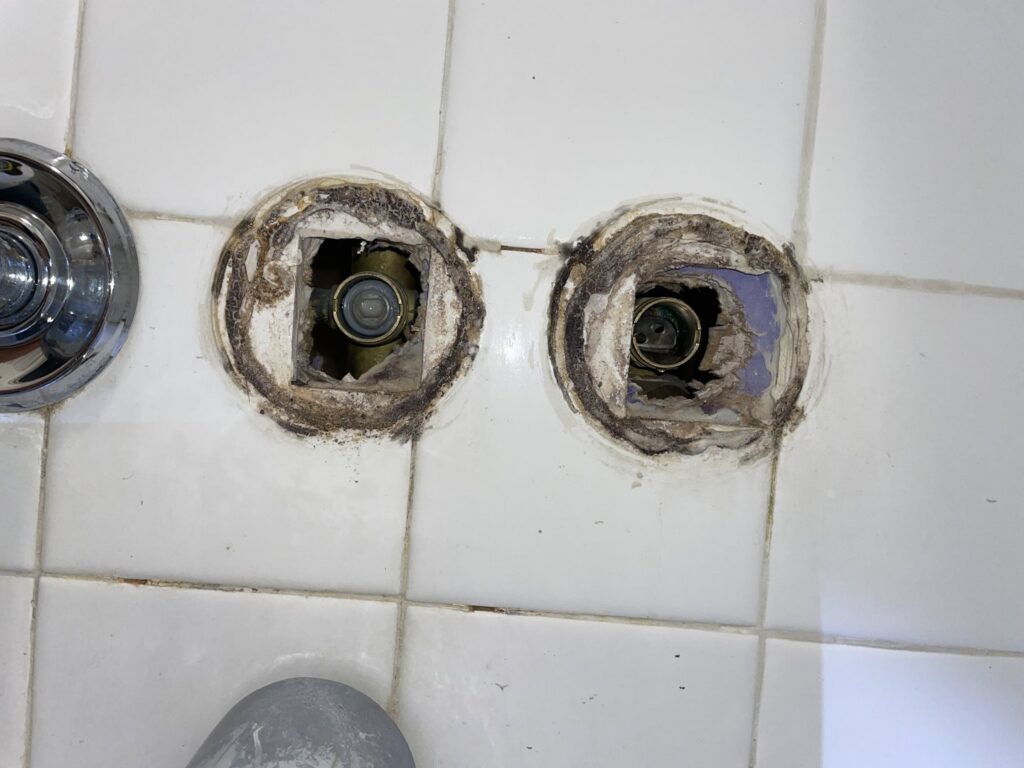 Mold and water damage visible around shower valve openings, indicating a leak repair and restoration by Hull Plumbing, Inc. in Oklahoma City, OK.