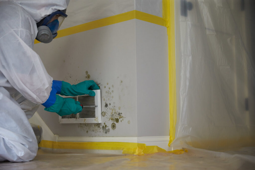 A ServiceMaster DSI specialist in a hazmat suit performing mold remediation on a wall vent in Maple Grove, MN.