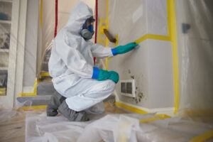 A ServiceMaster DSI specialist in a hazmat suit inspecting mold on a wall during remediation in Champaign, IL