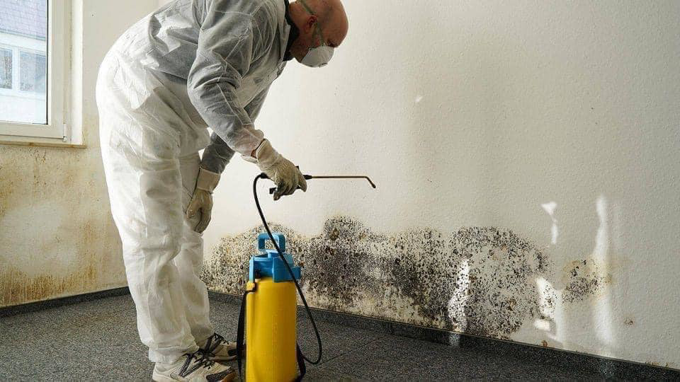 A technician in protective gear performing mold remediation on a wall, a service provided by Beacon Restoration and Cleaning, a water damage specialist in Birmingham, AL.