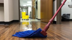 A blue mop on a wet, shiny floor with a cleaning cart in the background, showing work by Le Fine Cleaning in South Bend, IN.