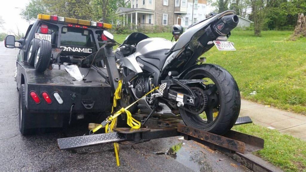 A silver and black sport motorcycle being loaded onto a flatbed tow truck by Whitelock Towing in Baltimore, MD.