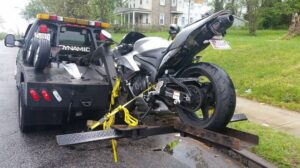 A silver and black sport motorcycle being loaded onto a flatbed tow truck by Whitelock Towing in Baltimore, MD.
