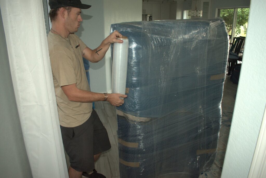A professional mover applying plastic wrap to furniture for protection by Moving Pros LLC in Surprise, AZ.
