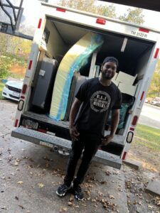 A friendly mover from E.L.I Movers LLC standing at the back of a loaded moving truck in Houston, TX, ready for transport.