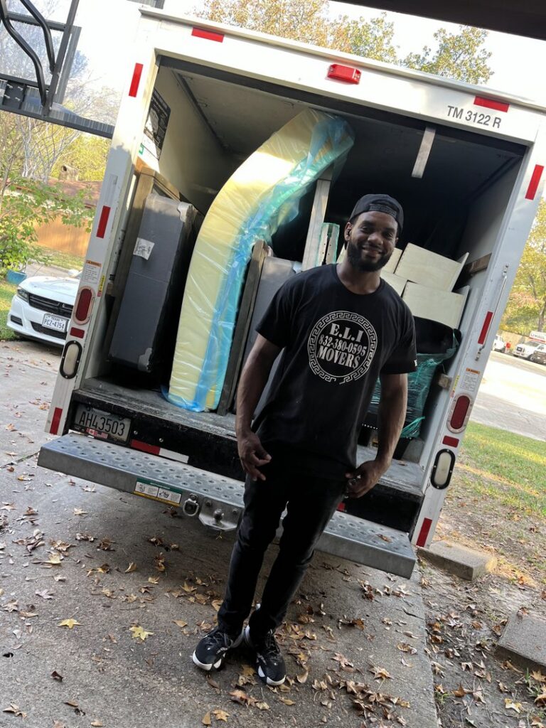 A friendly mover from E.L.I Movers LLC standing at the back of a loaded moving truck in Houston, TX, ready for transport.
