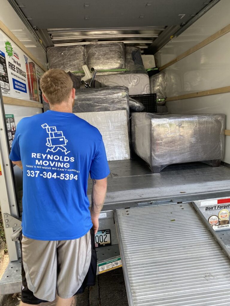 A mover from Reynolds Moving in Baton Rouge, LA, standing at the back of a moving truck filled with wrapped furniture and boxes